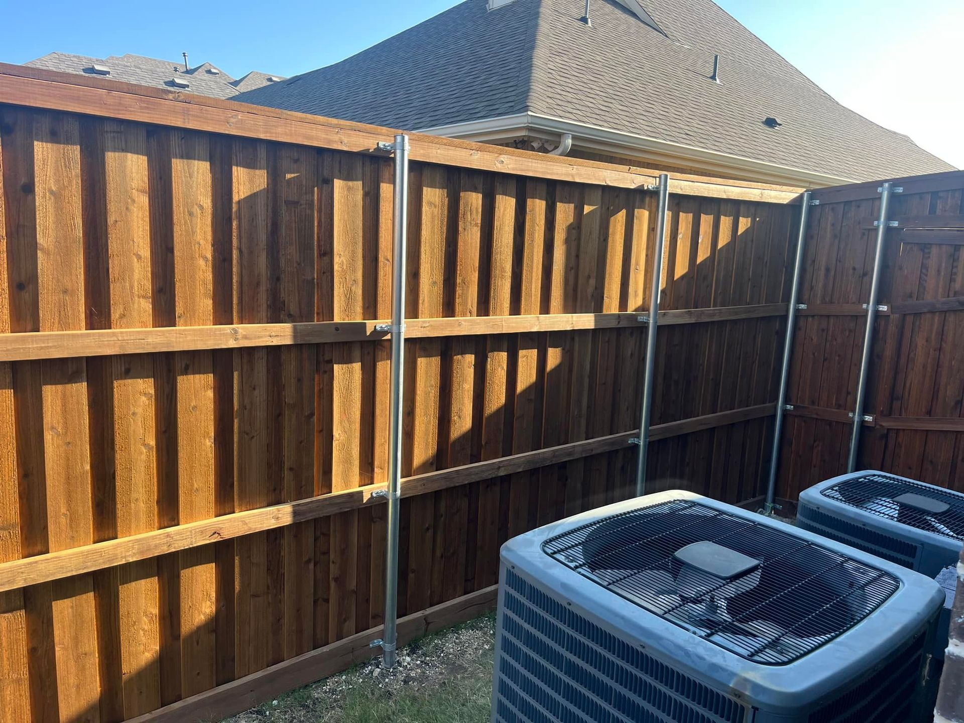 Wooden backyard fence beside two outdoor HVAC units in bright sunlight