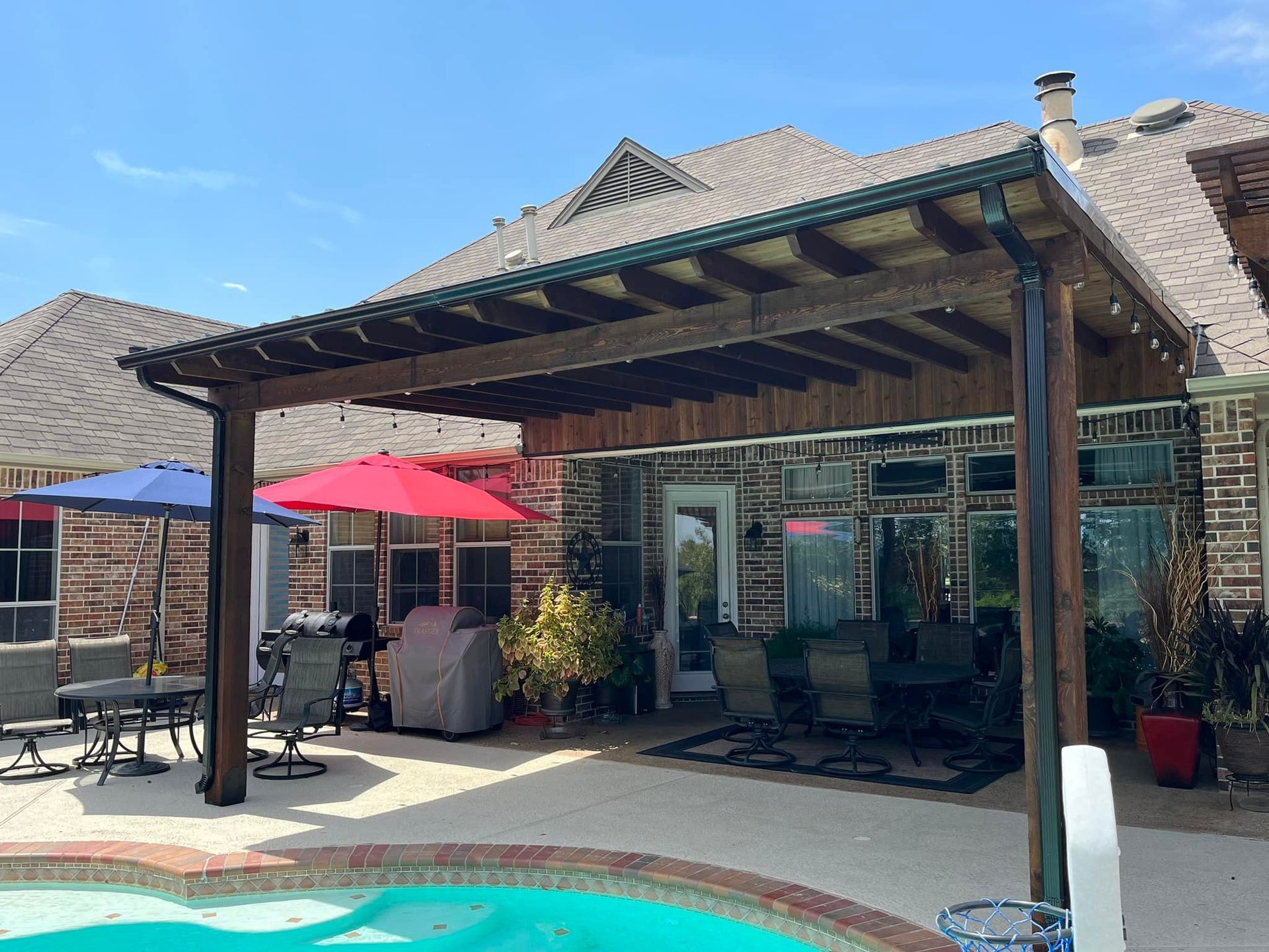 Patio with a pool, red umbrellas, and a shaded brick building with glass doors