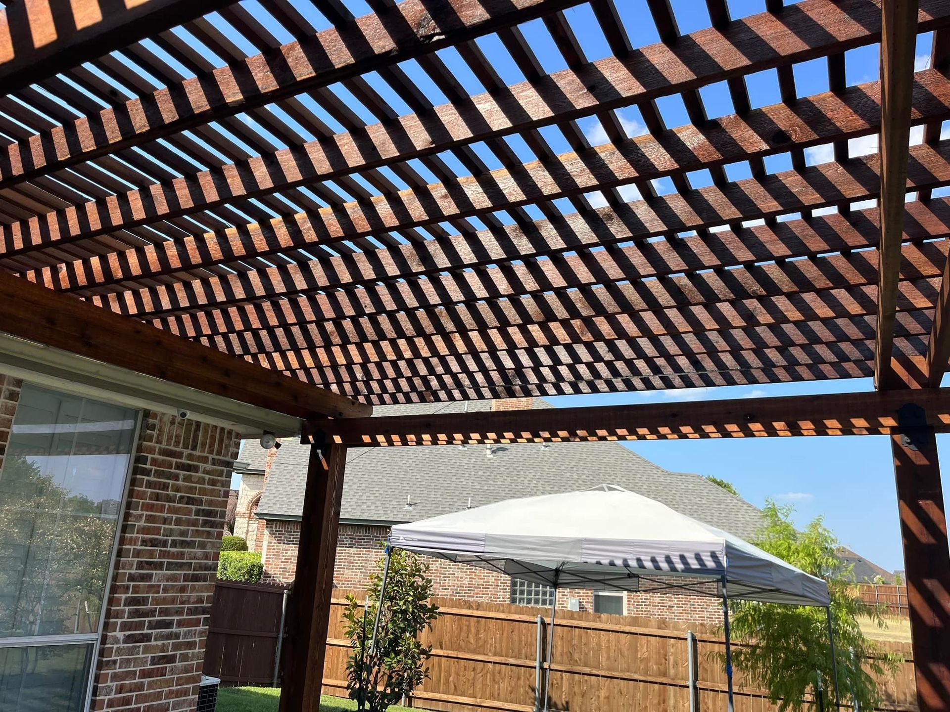 Backyard patio with wooden pergola, brick columns, and a white umbrella under a blue sky