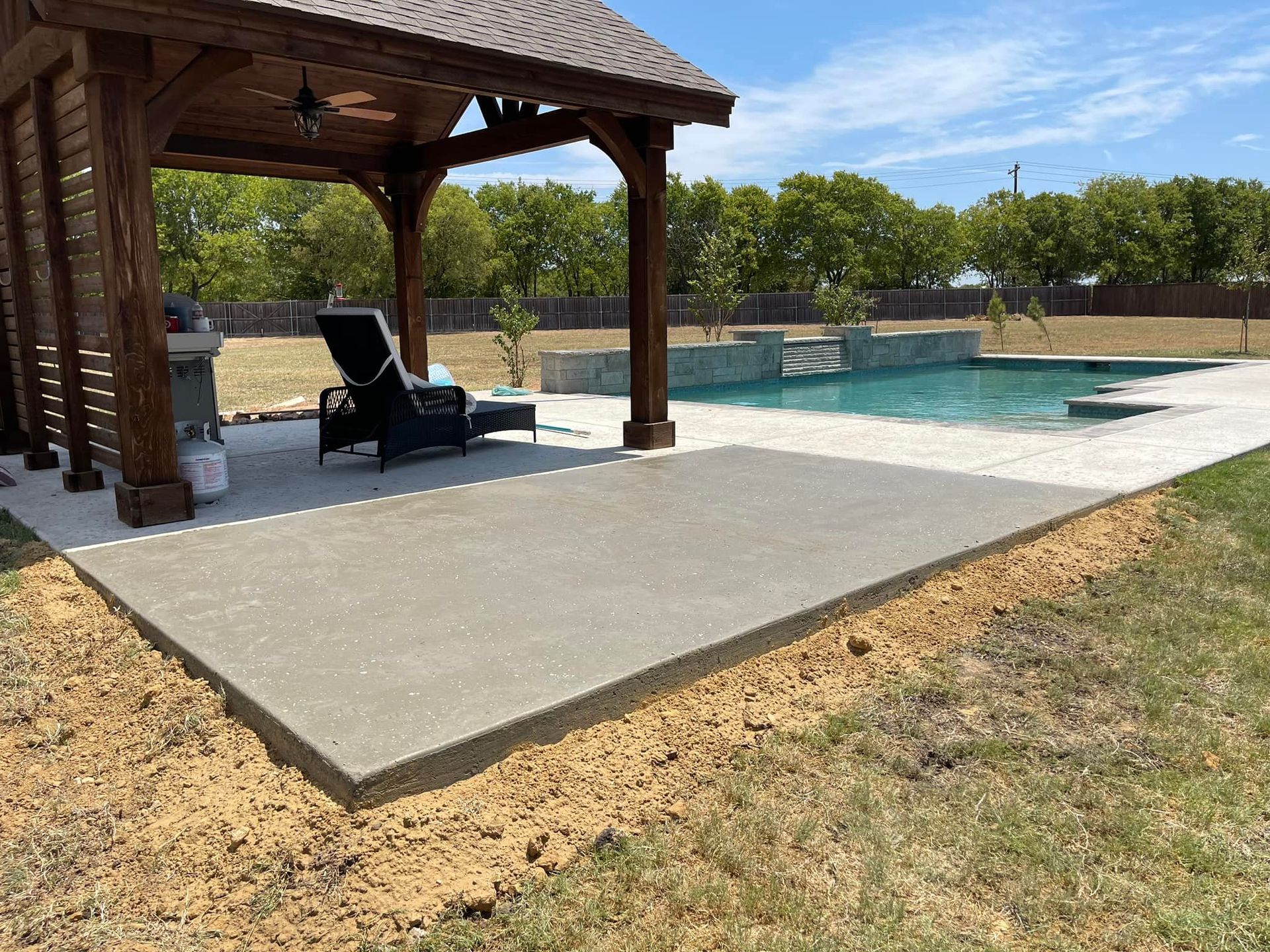 Backyard pool with a wooden pavilion, lounge chairs, and a concrete patio beside the water