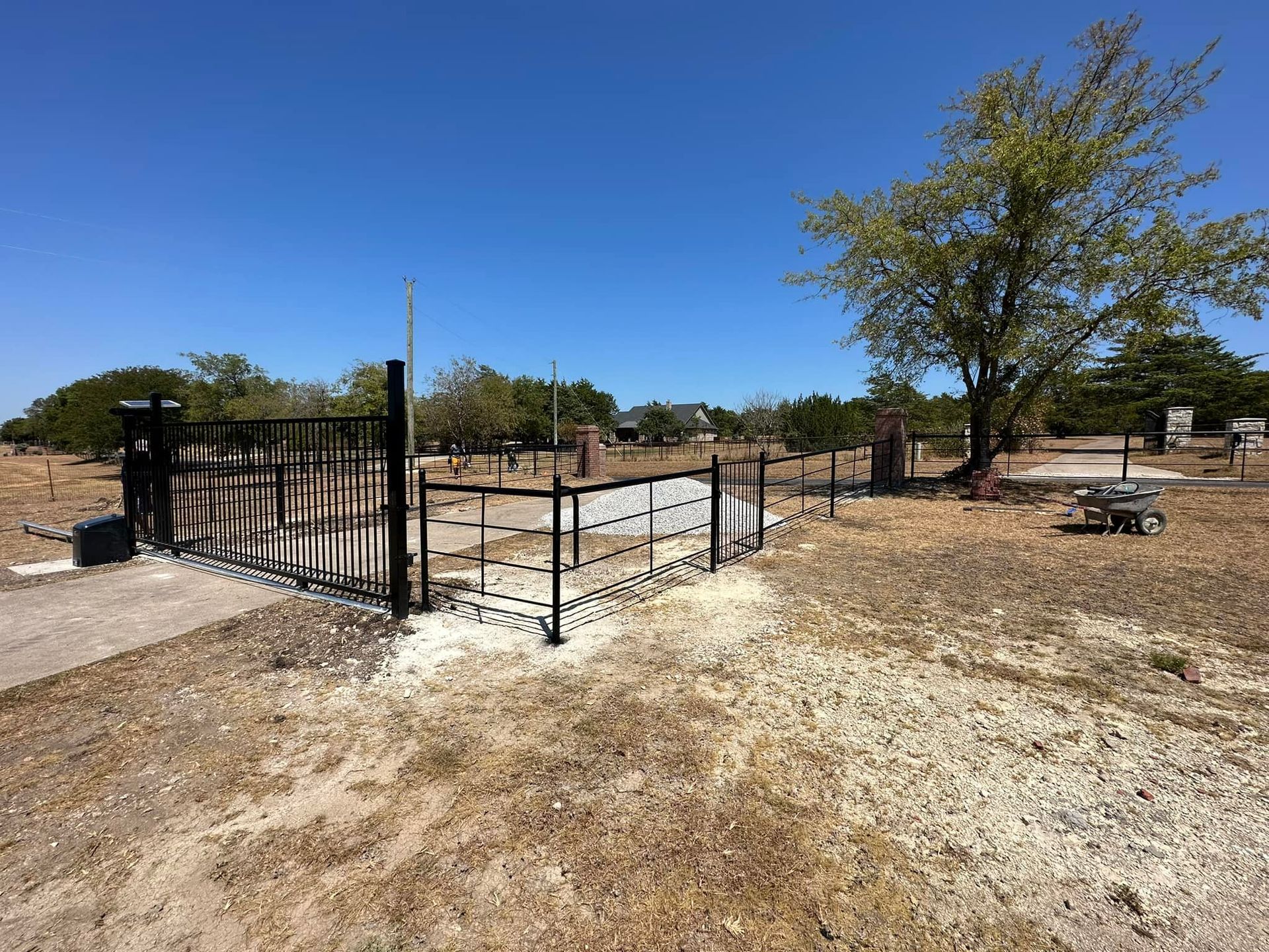Black metal fenced enclosure in a dry, open park under a clear blue sky