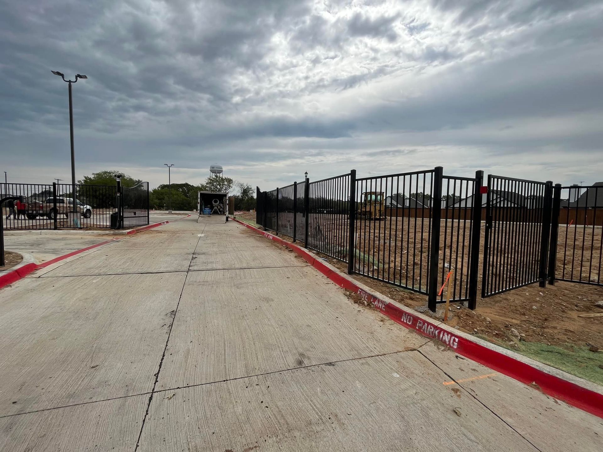 Empty paved road beside black metal fence under cloudy sky