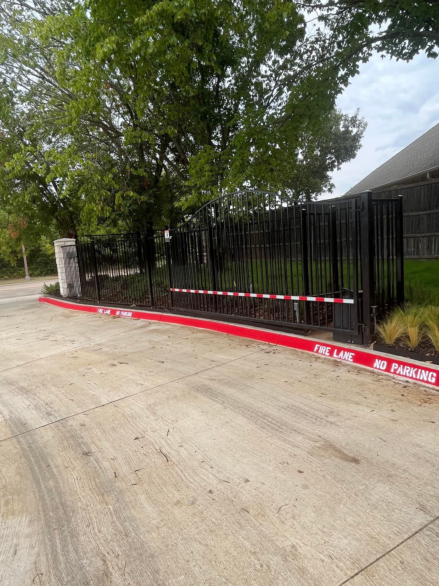 Red curb along a concrete driveway beside a black fence and trees near a building