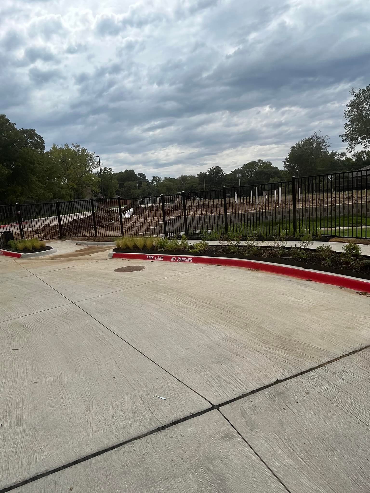Collapsed black metal fence along a curb under a cloudy sky at a parking lot entrance
