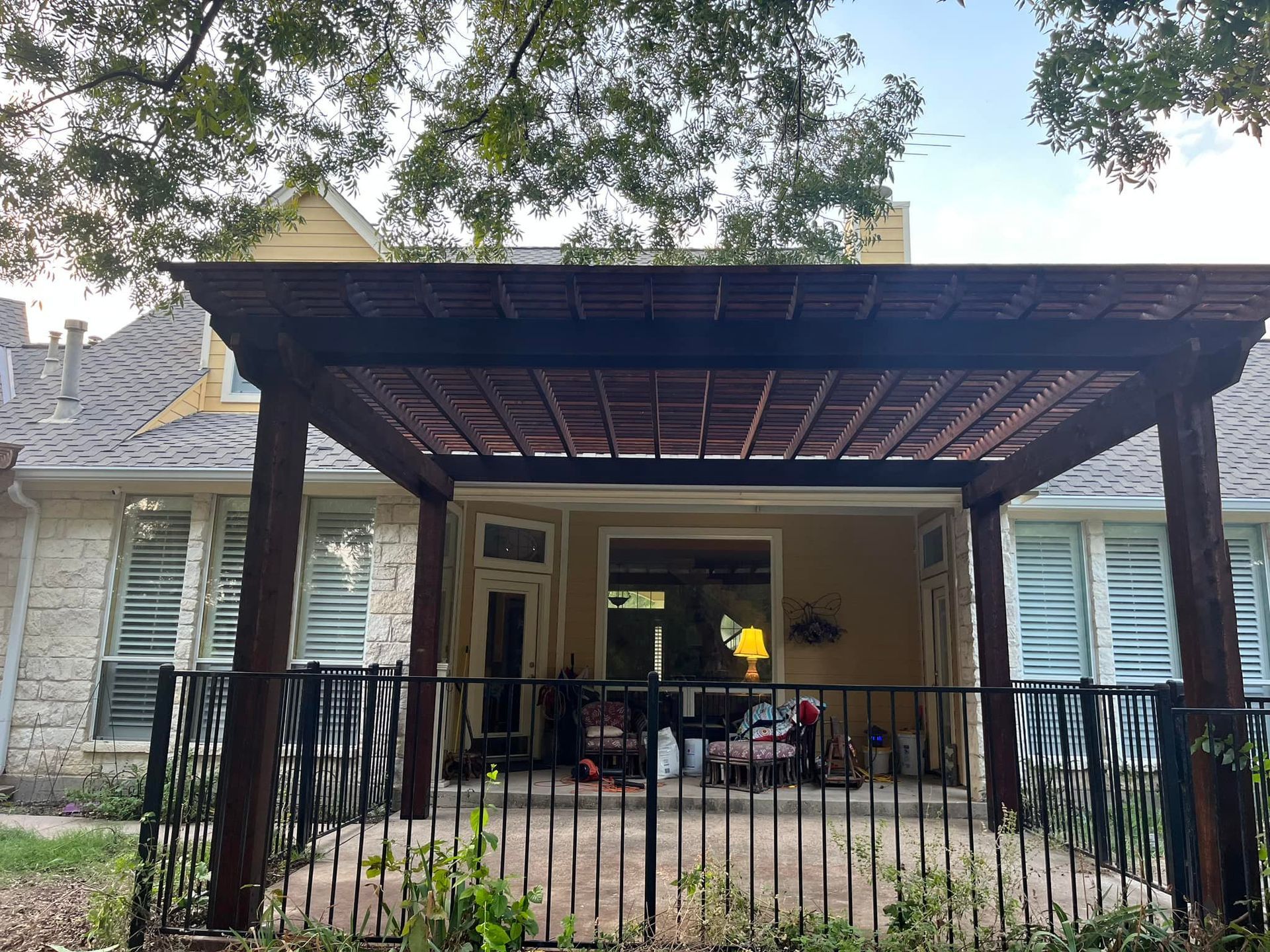 Covered patio with black railing, outdoor furniture, and a lit lamp in front of a house