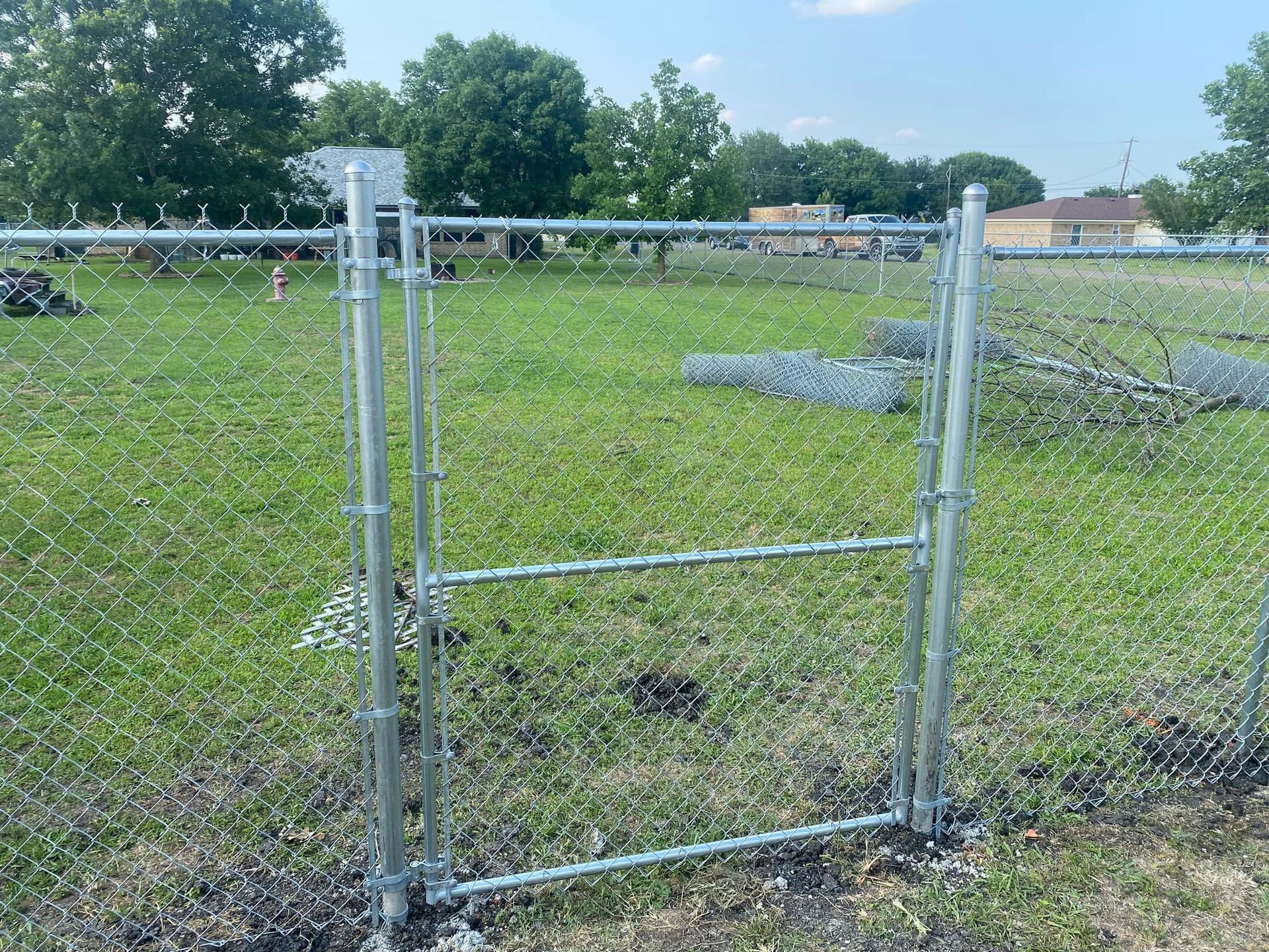 Chain-link gate in a grassy field with trees and a building in the background