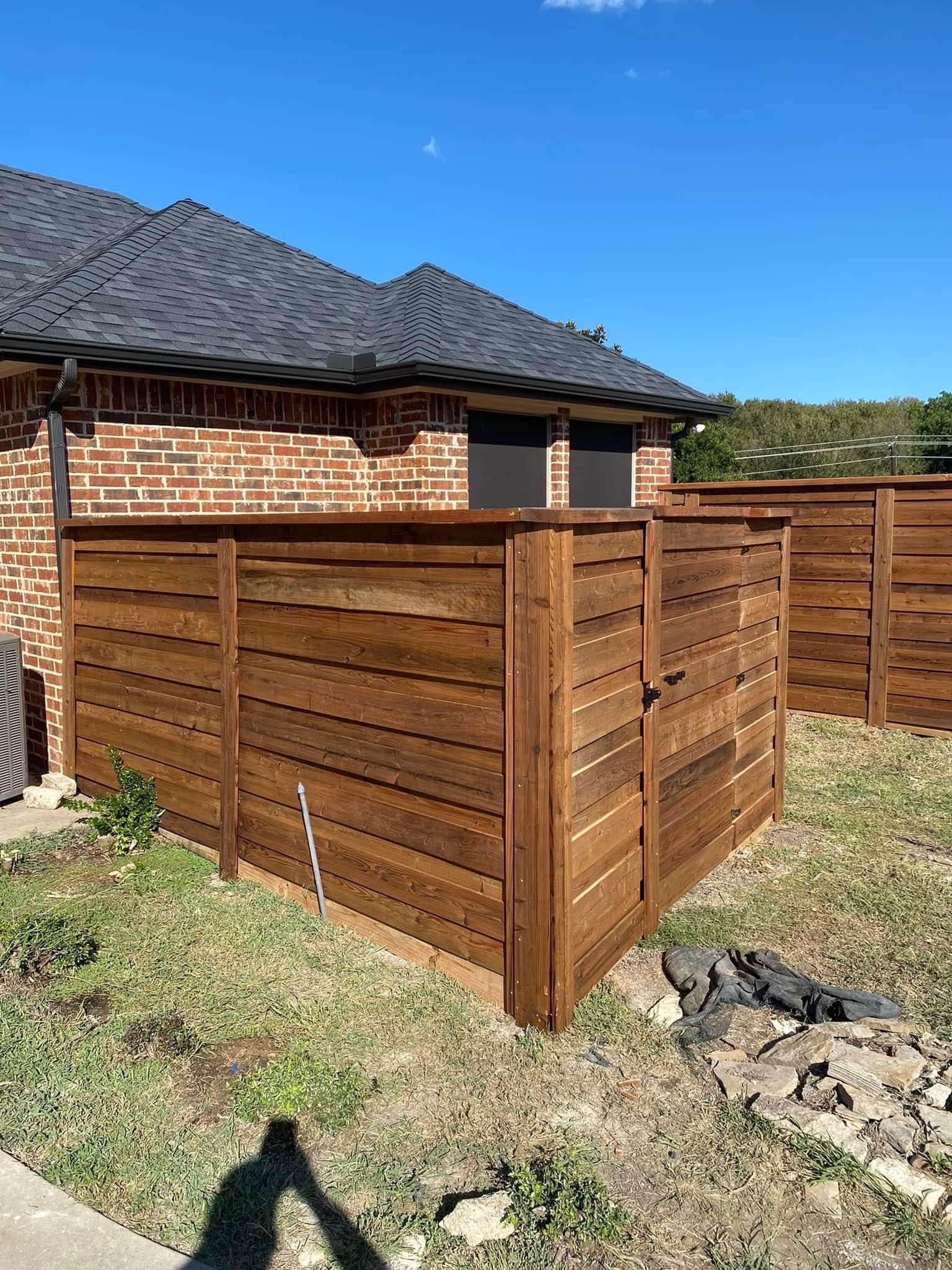 Wooden fenced enclosure in a backyard beside a brick house on a sunny day