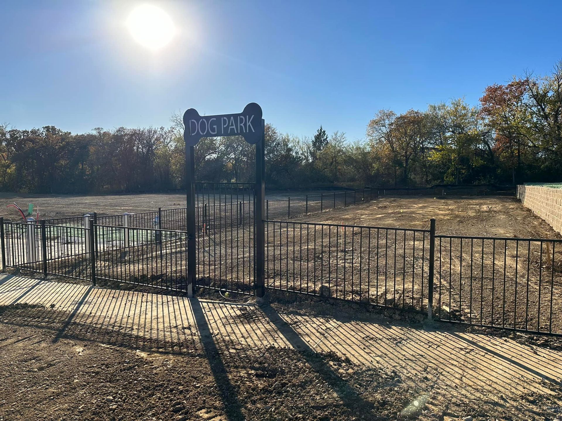 Sunlit fenced playground entrance with a blue sign and leafless trees beyond