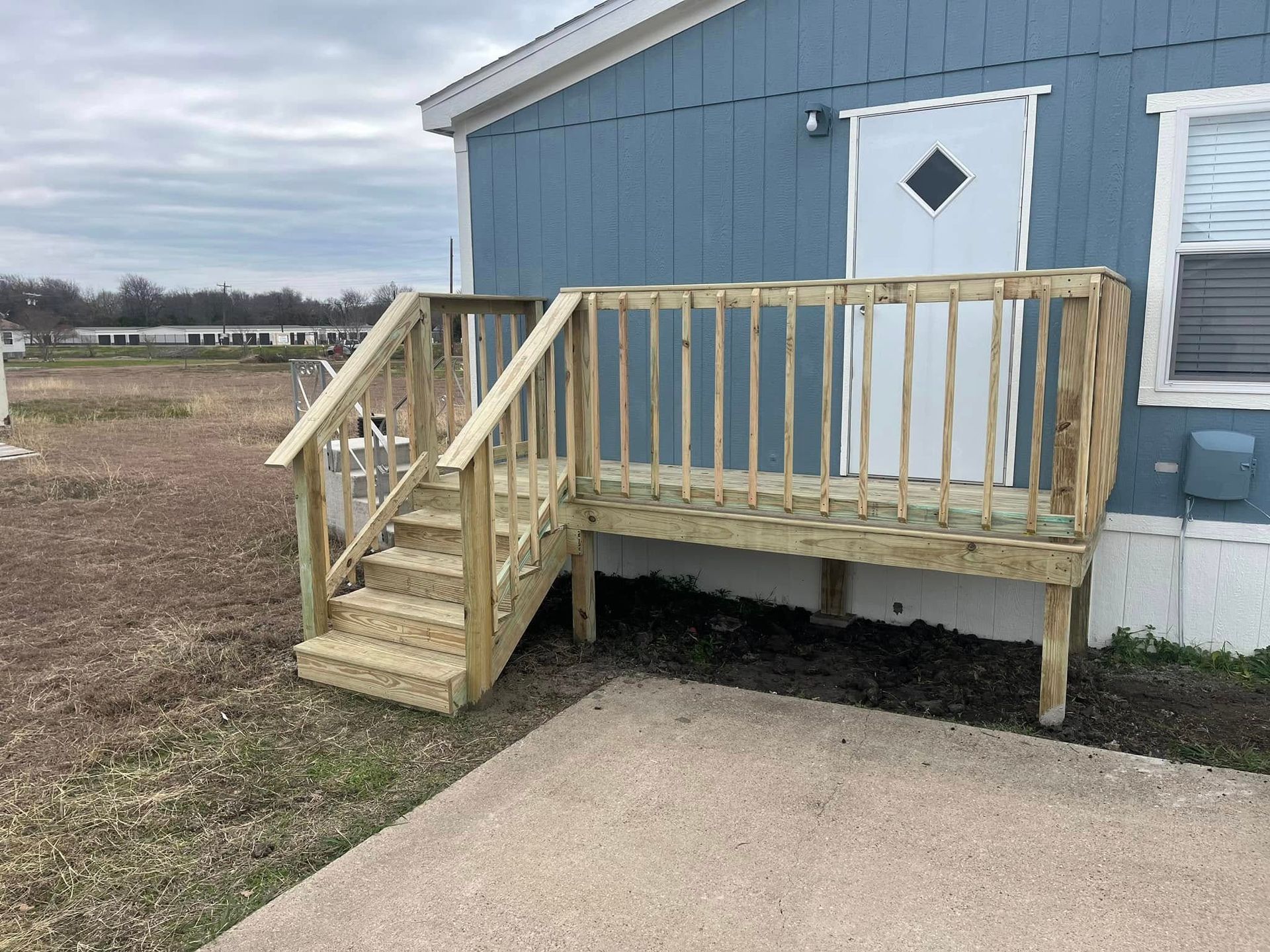 Small wooden wheelchair ramp with railing beside a blue house and white door