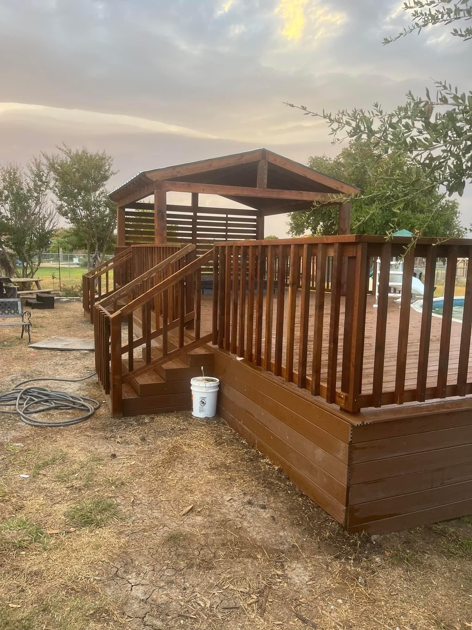 Wooden ramp and deck with railings beside a gazebo in a yard at sunset