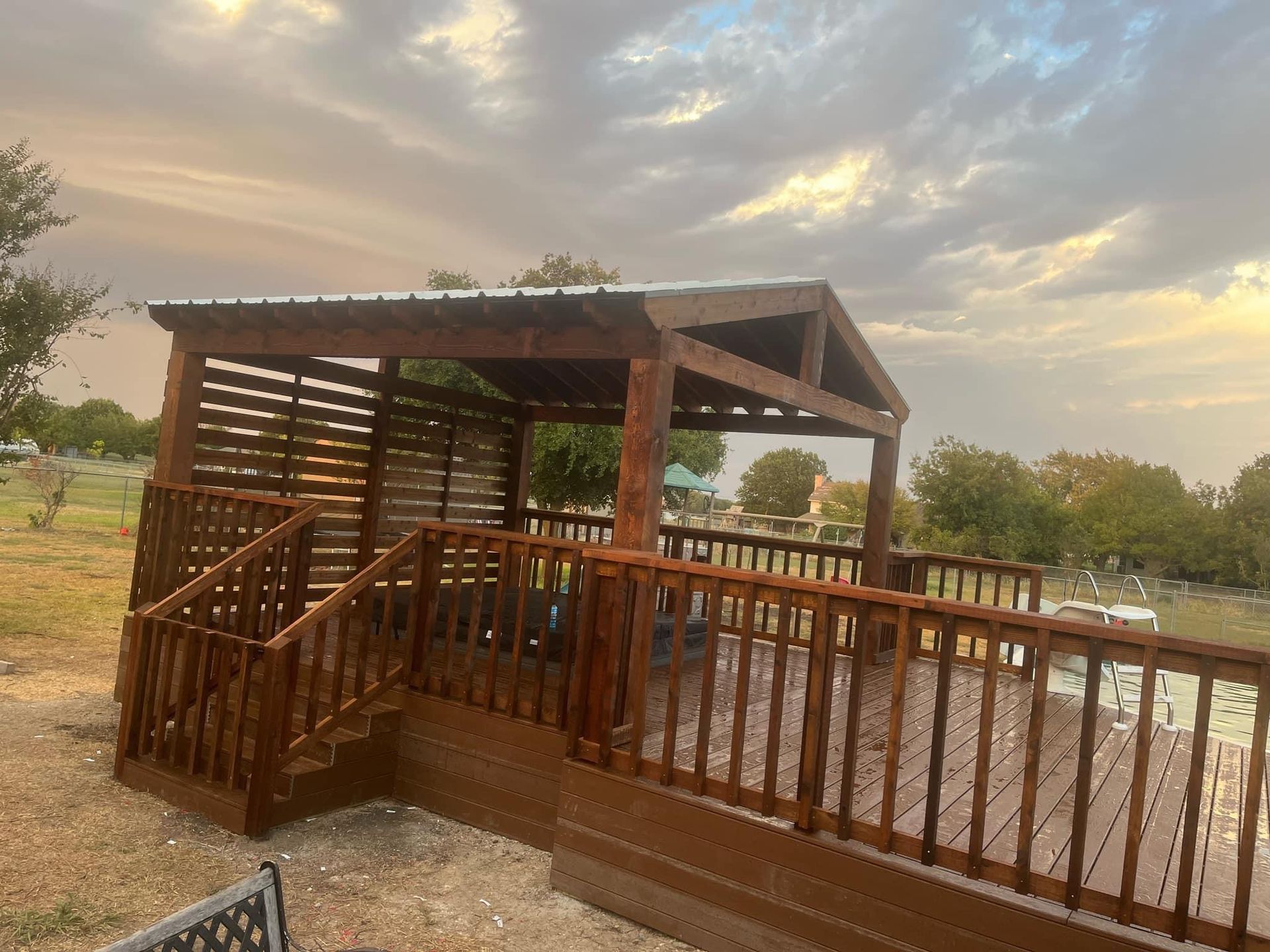 Wooden gazebo with ramp and railing beside a pond at sunset