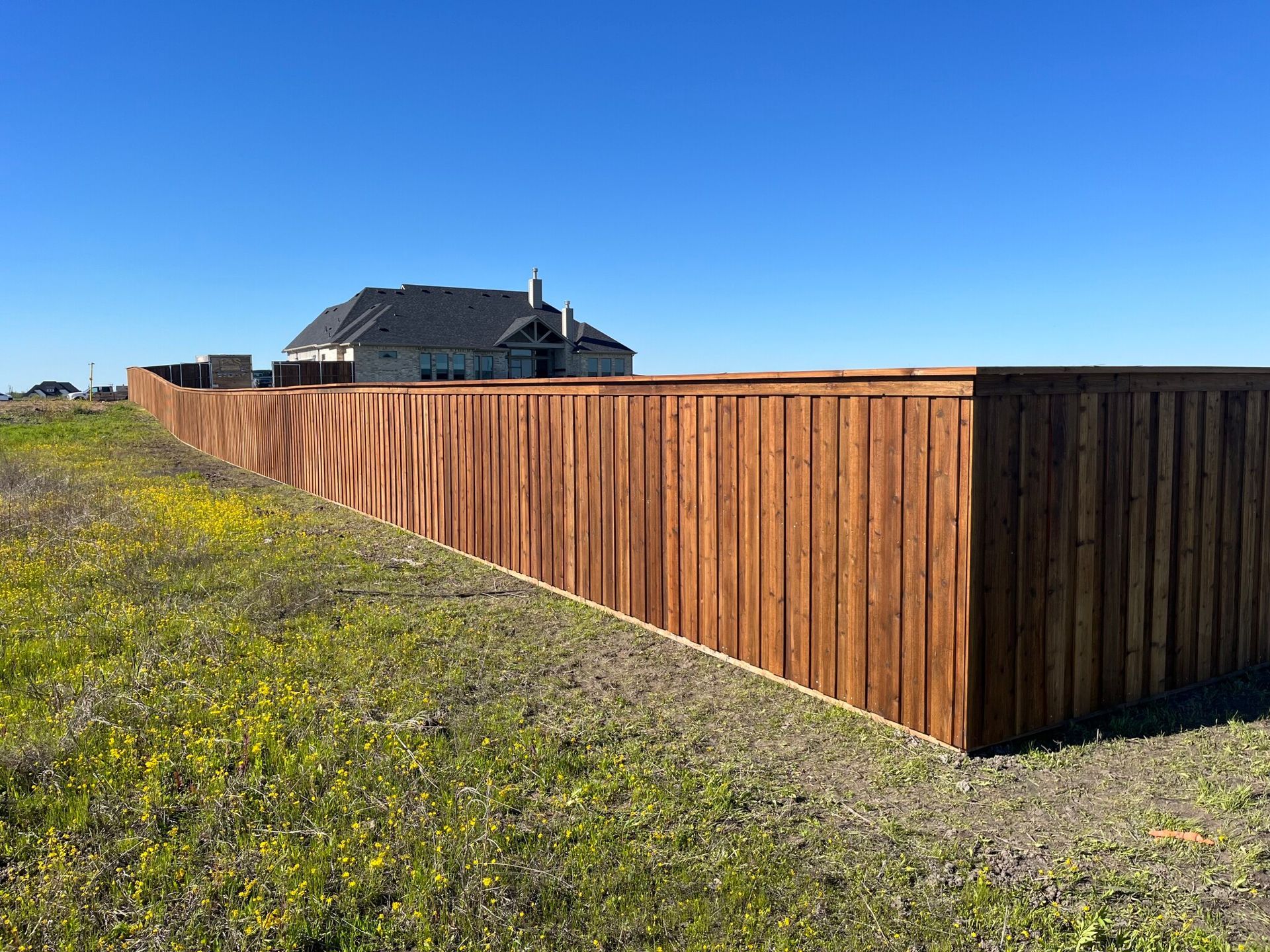 Wooden privacy fence around a yard under a clear blue sky, with a house in the background