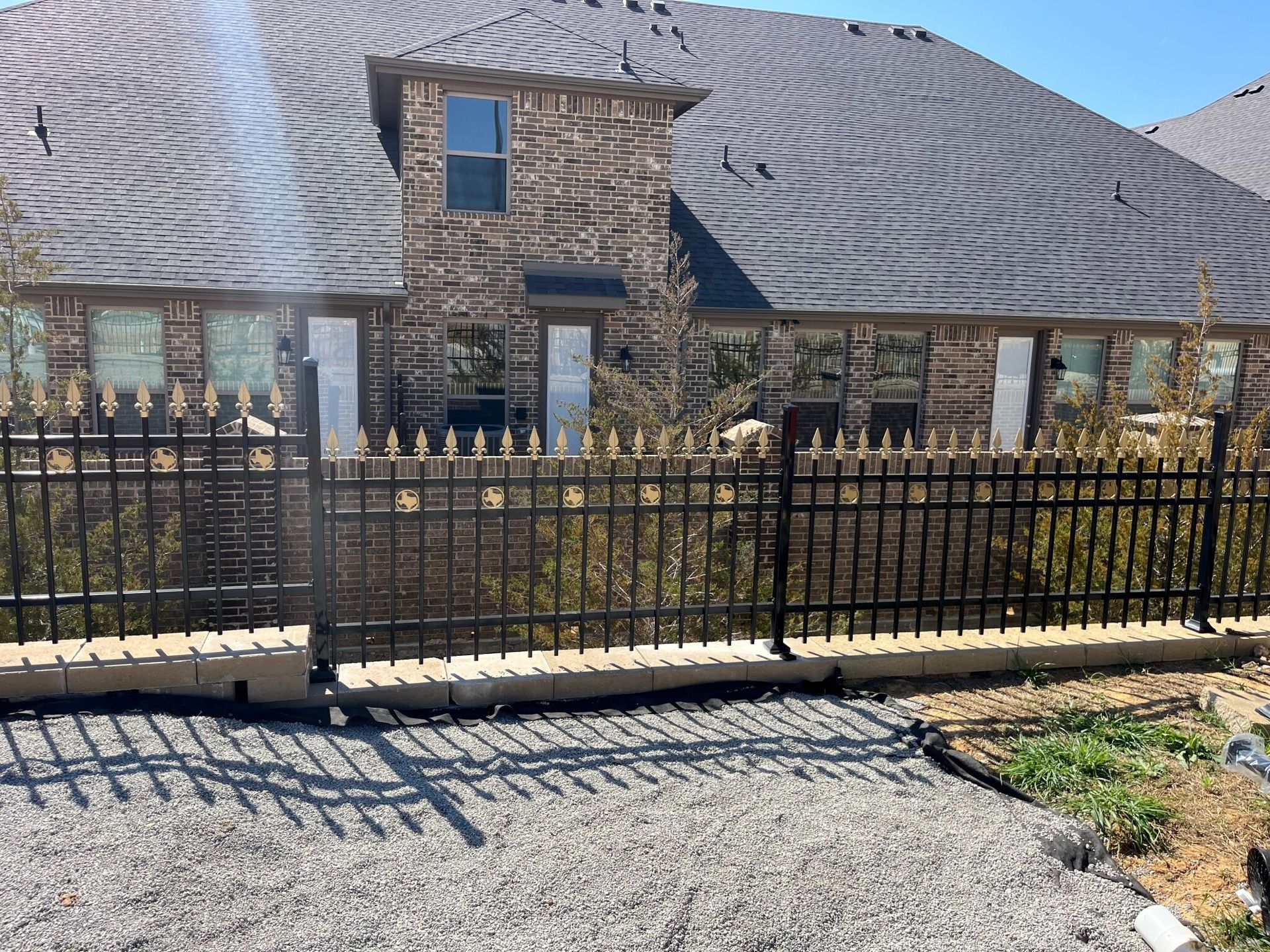 Stone house with a black metal fence in front of a curved, striped hillside.