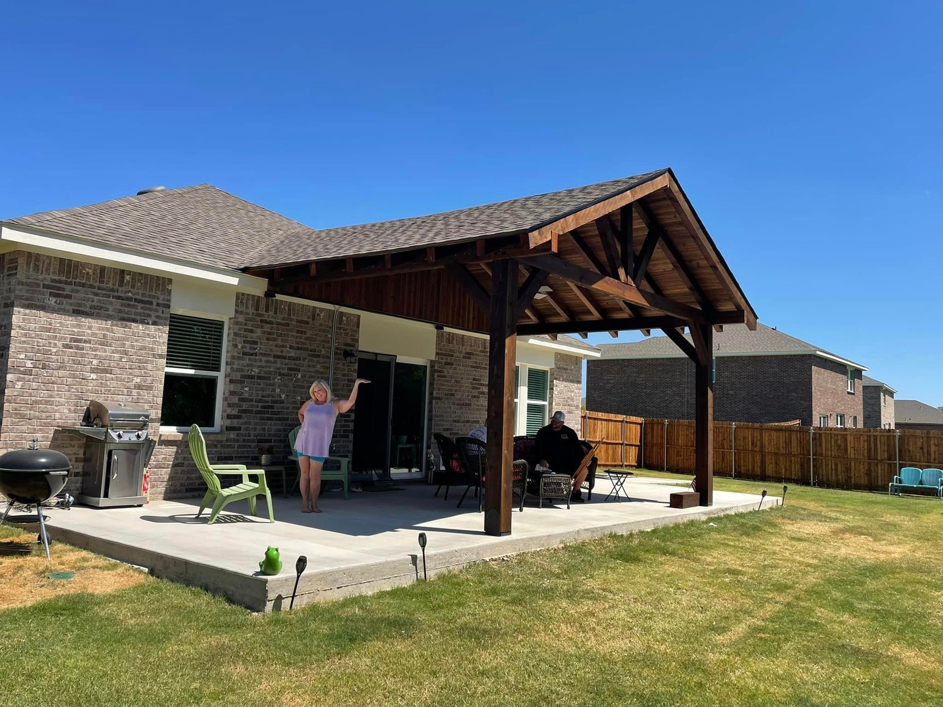 Patio with covered grill area, chairs, and a person standing near the house under a clear blue sky