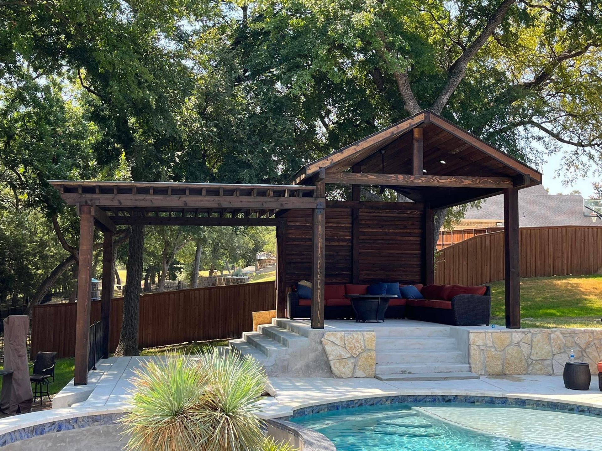 Backyard gazebo with covered seating, stone patio, and trees in the background