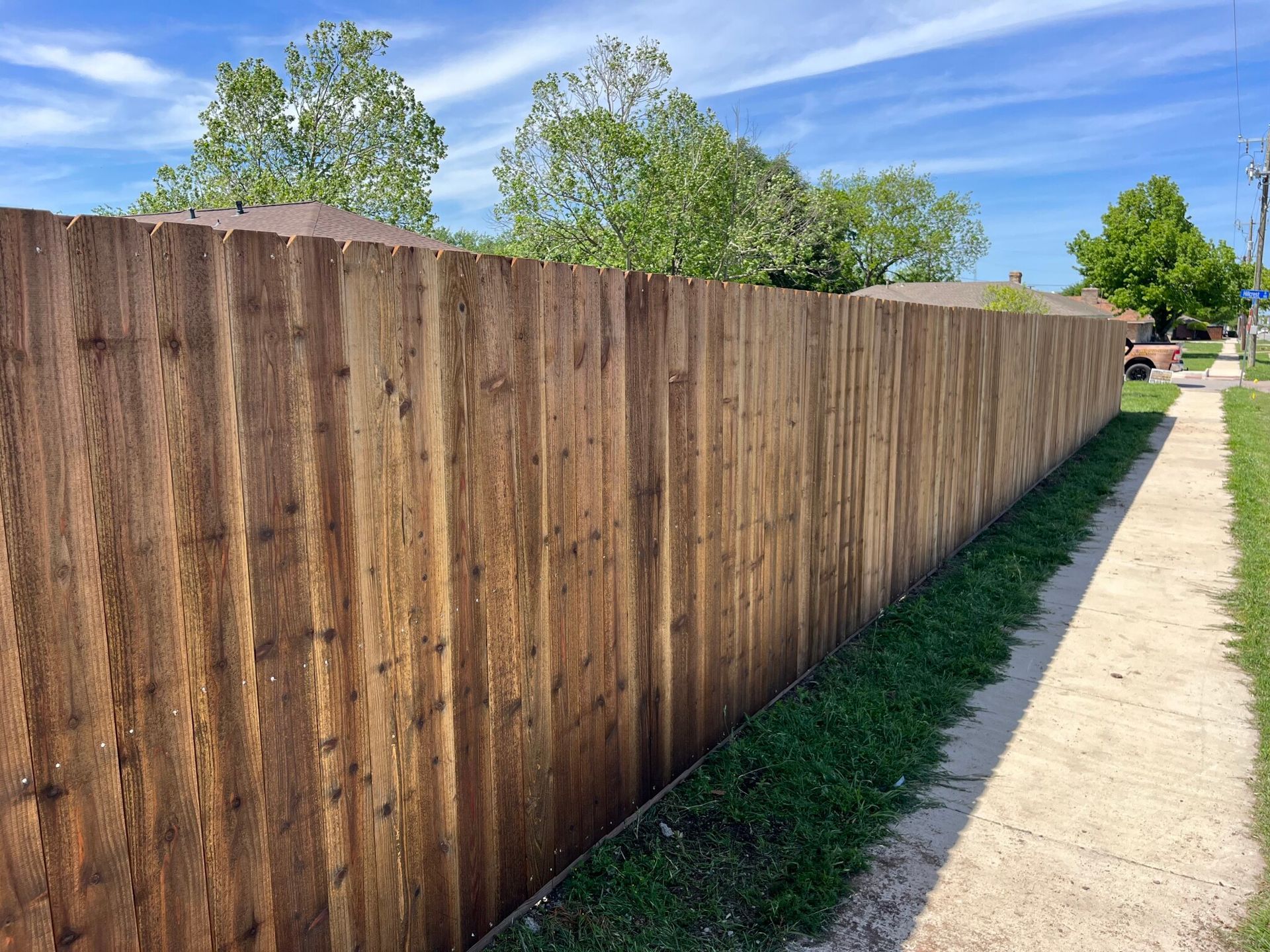 Long wooden fence beside a sidewalk under a blue sky on a sunny day