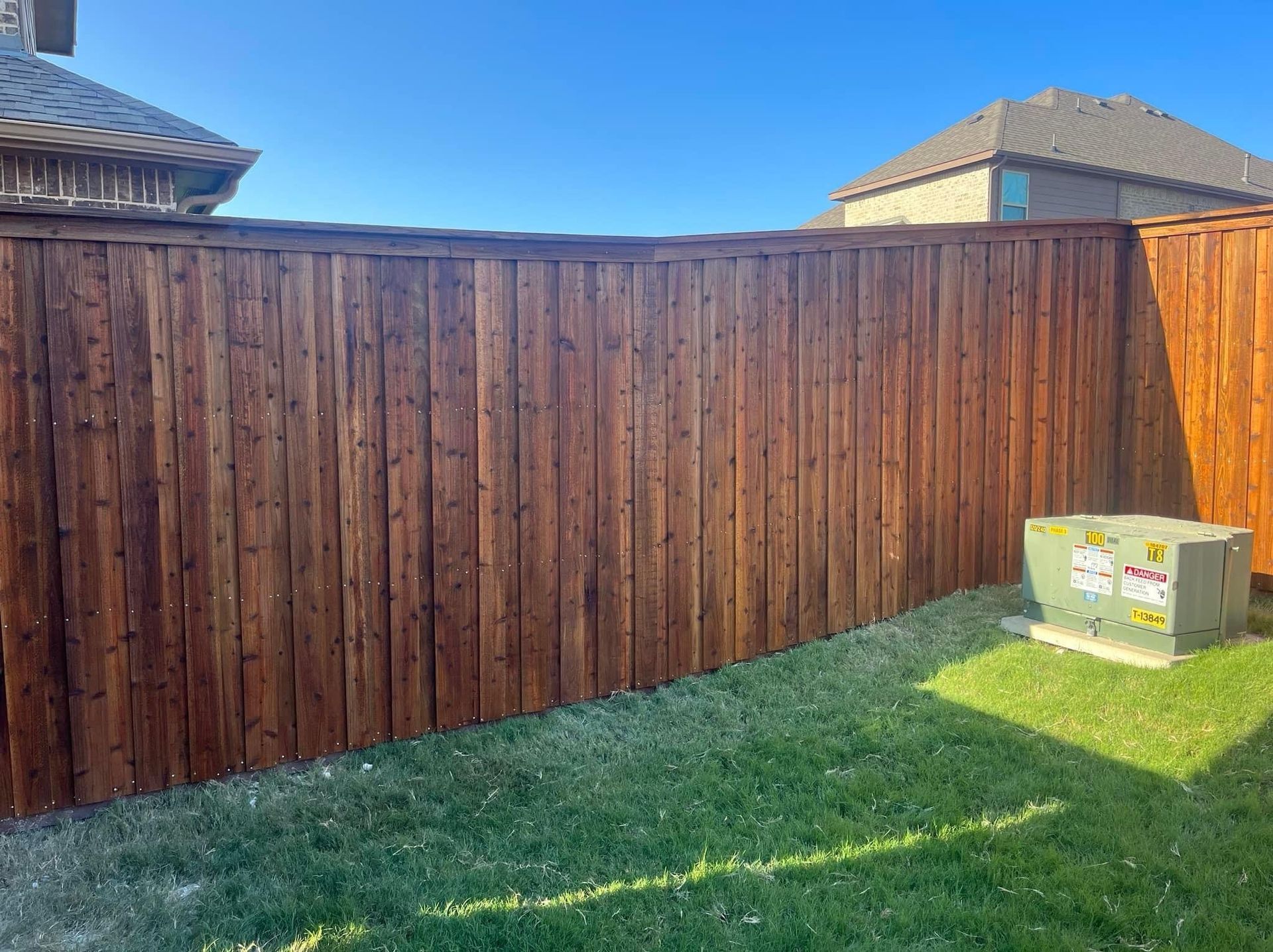 Backyard with a tall wooden fence, green grass, and a cardboard box near the right side.