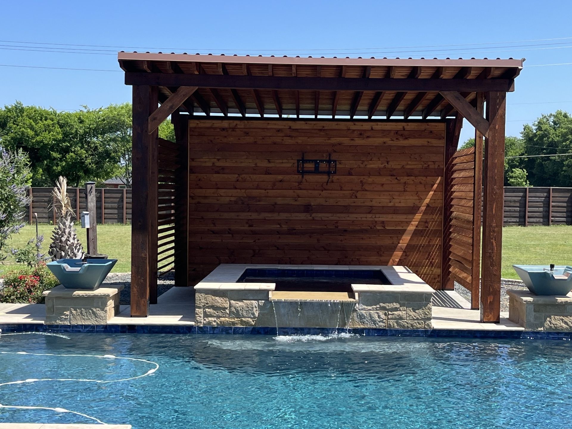 Wooden poolside cabana with shaded daybed beside a blue swimming pool