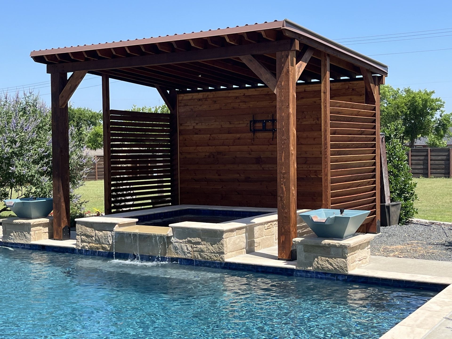 Poolside wooden cabana with stone bar and stools beside a blue swimming pool