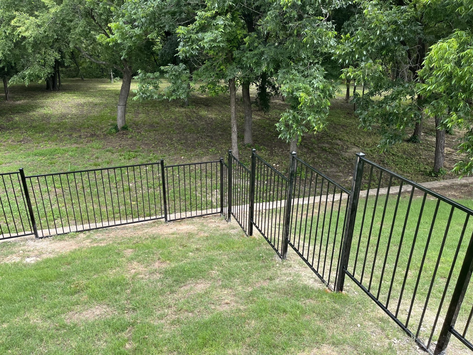 Black metal fence along a grassy slope in a wooded park area