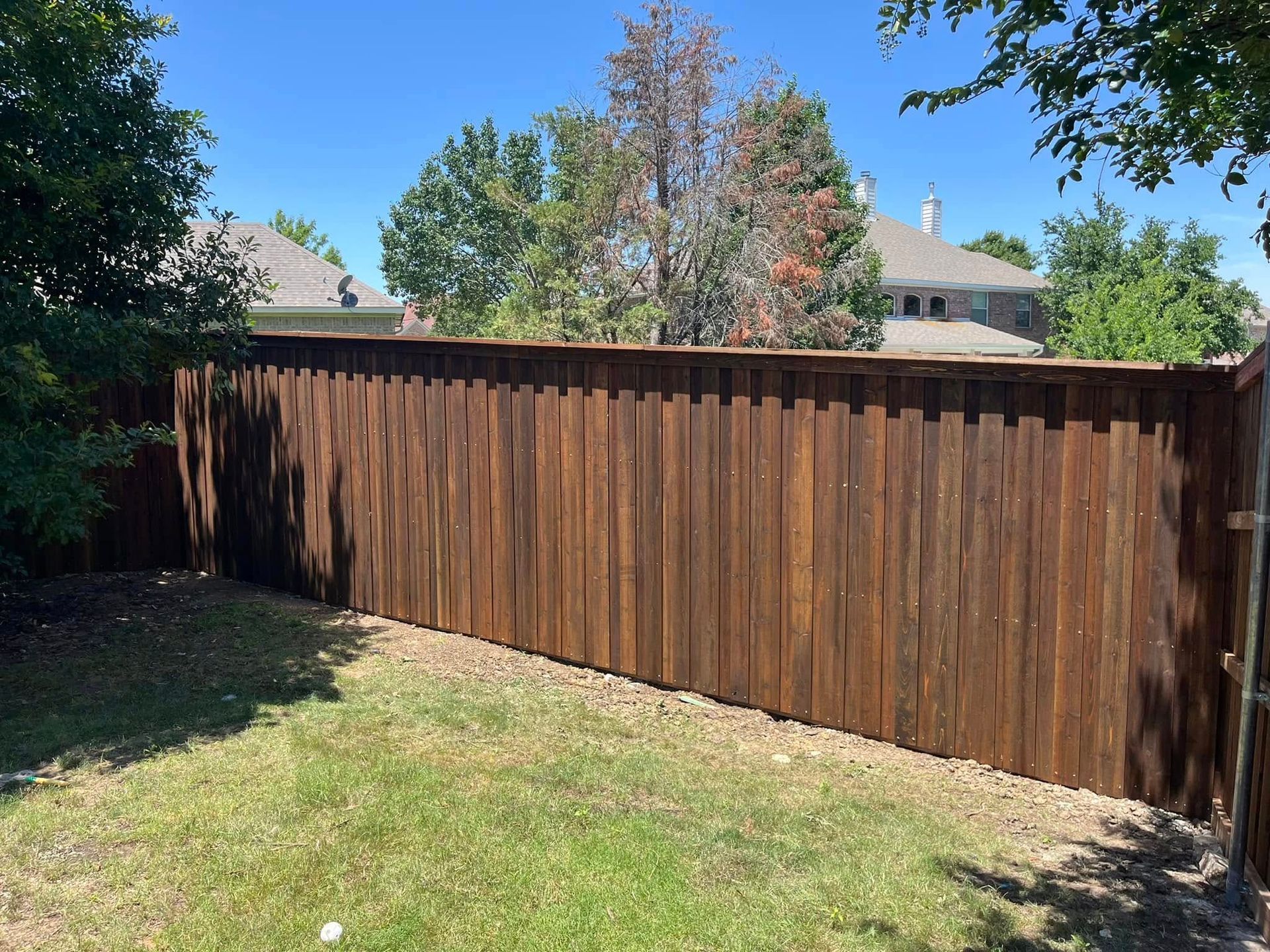 Weathered wooden fence along a grassy backyard with trees and houses in the background