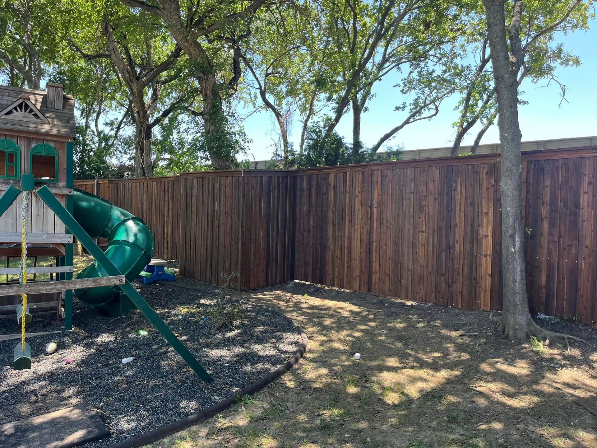 Backyard with wooden fence, trees, and a green playground slide on the left.
