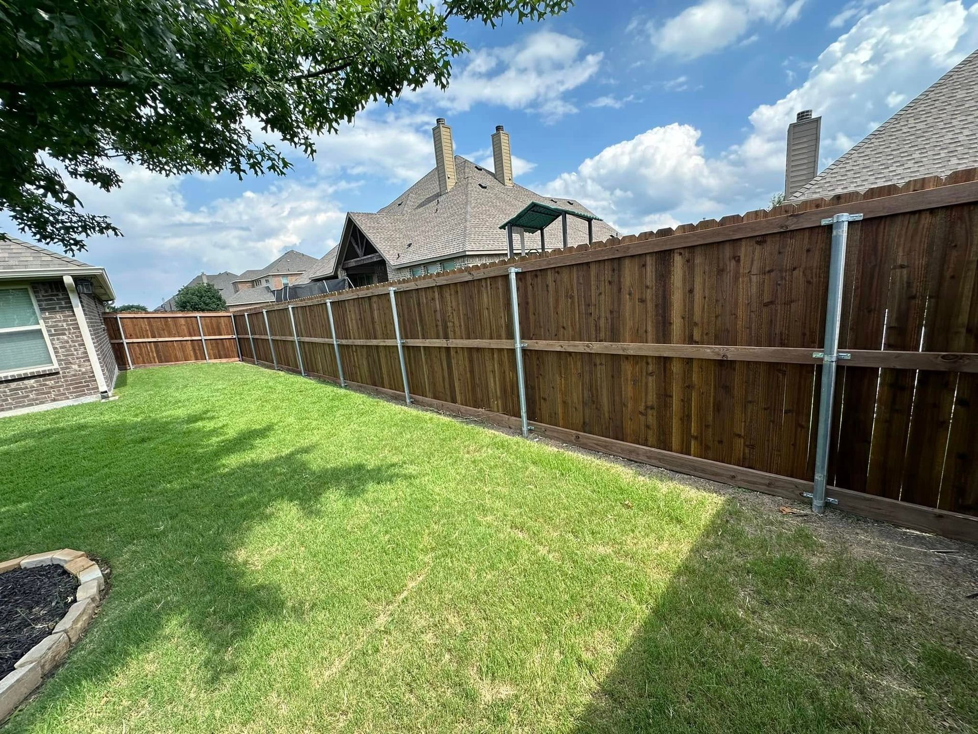 Backyard with green lawn, wooden fence, trees, and a partly cloudy sky
