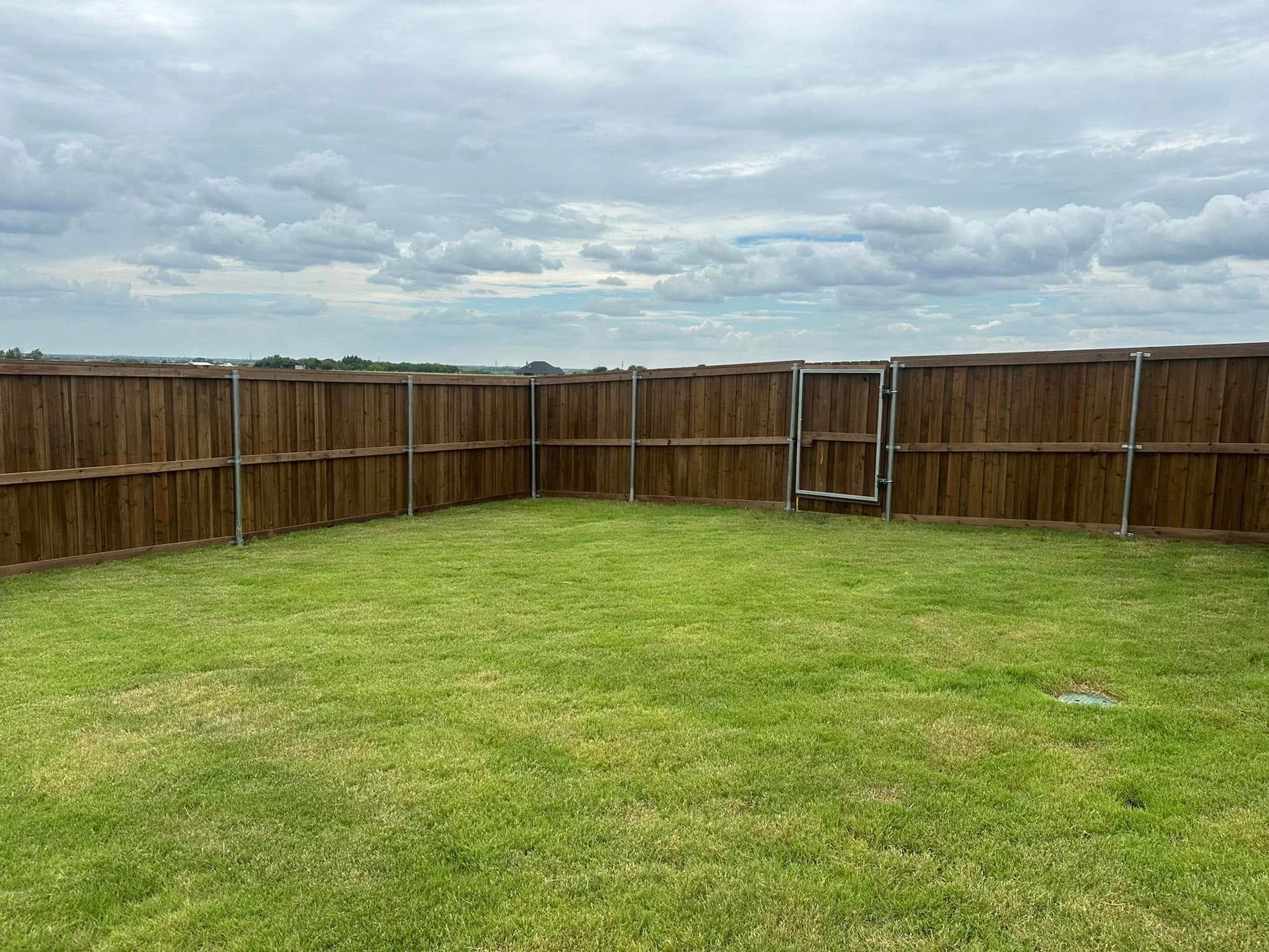 Grassy backyard enclosed by a wooden fence under a cloudy sky