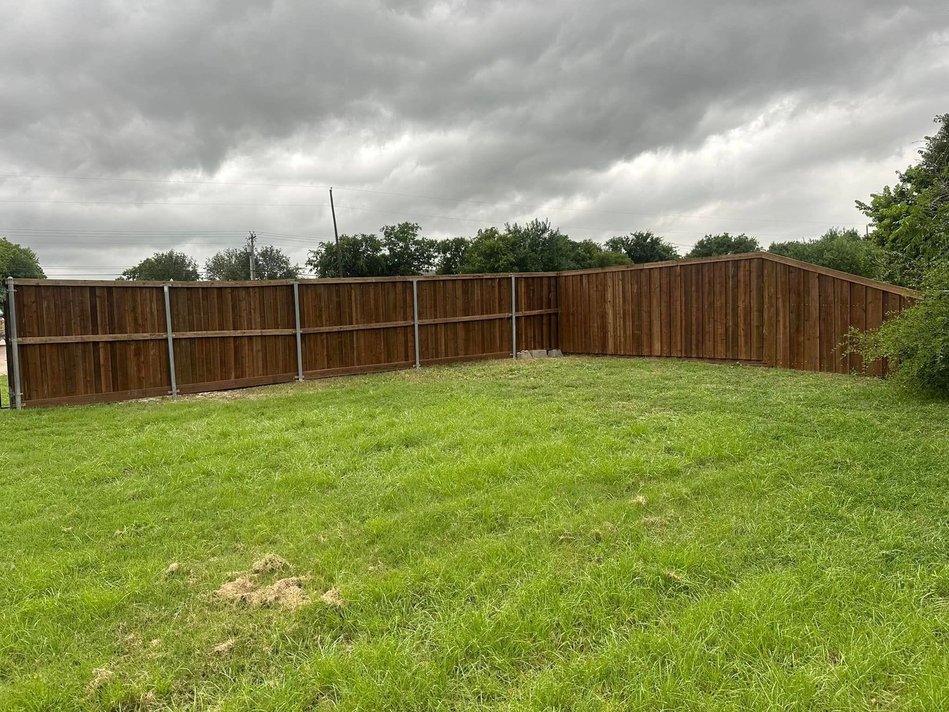 Backyard with green grass, a wooden fence, and cloudy overcast sky