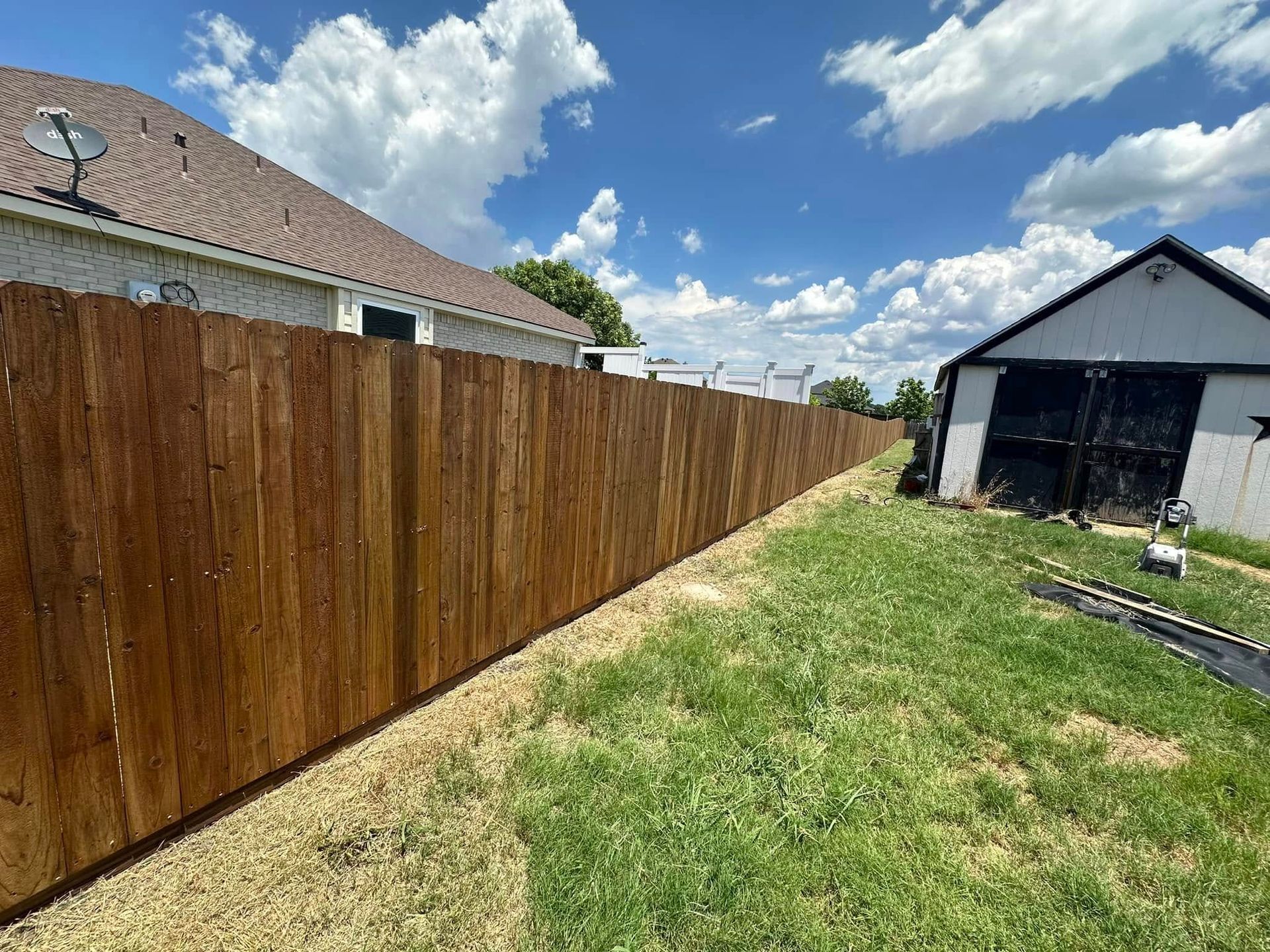 Long wooden fence beside a grassy yard under a blue, partly cloudy sky