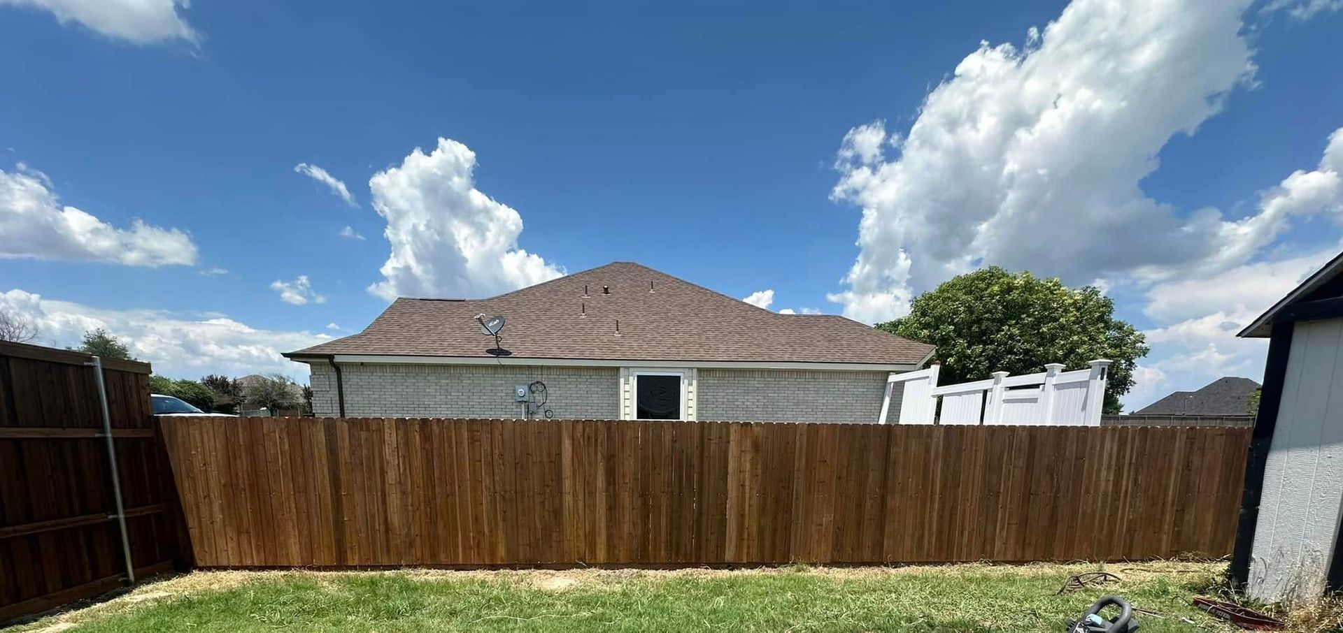 Backyard with a wooden fence, single-story house, and blue sky with clouds