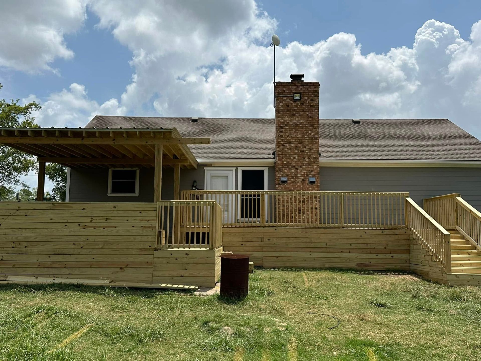 Single-story house with wooden deck, central brick chimney, and cloudy sky above