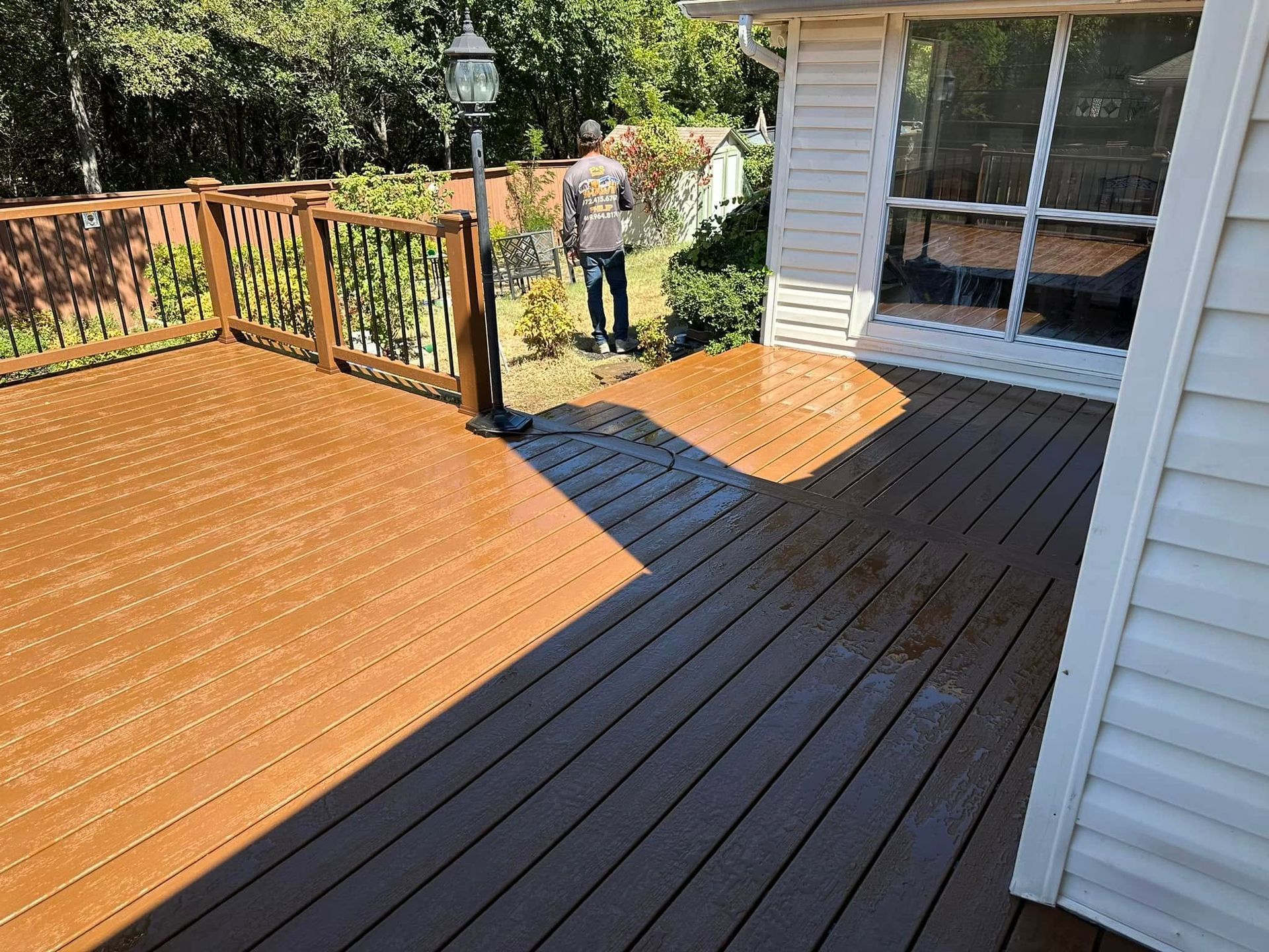 Wooden deck with railings beside a house, featuring a person standing near the far side.