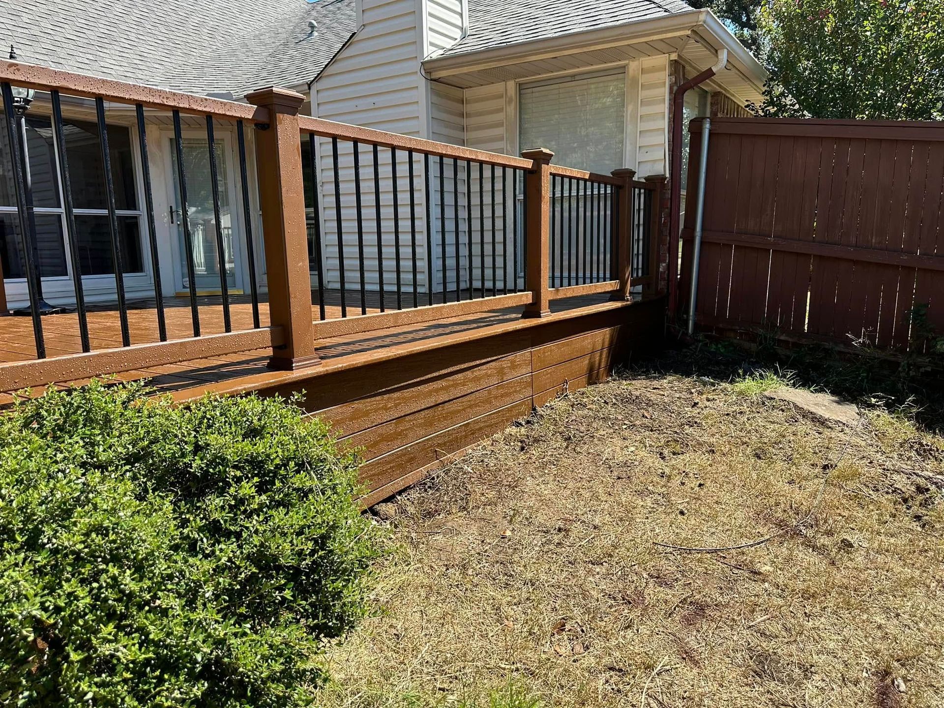 Backyard deck with black railing, brick posts, and a wooden fence beside a patchy lawn.