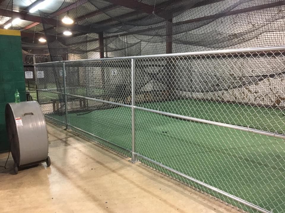 Indoor sports court with green turf, chain-link fencing, and a batting cage area