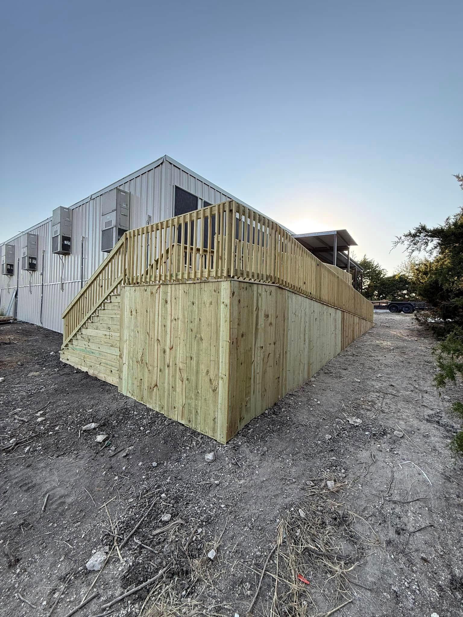 Wooden retaining wall and stairs beside a corrugated metal building on a gravel slope at sunset