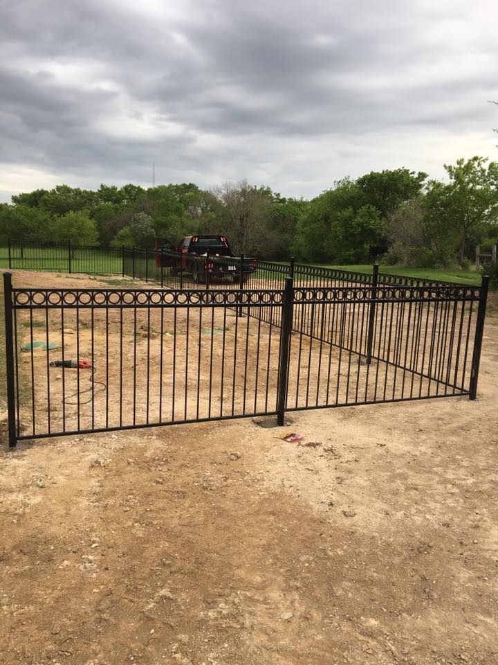 Black metal gate on a dirt road with trees and cloudy sky in the background