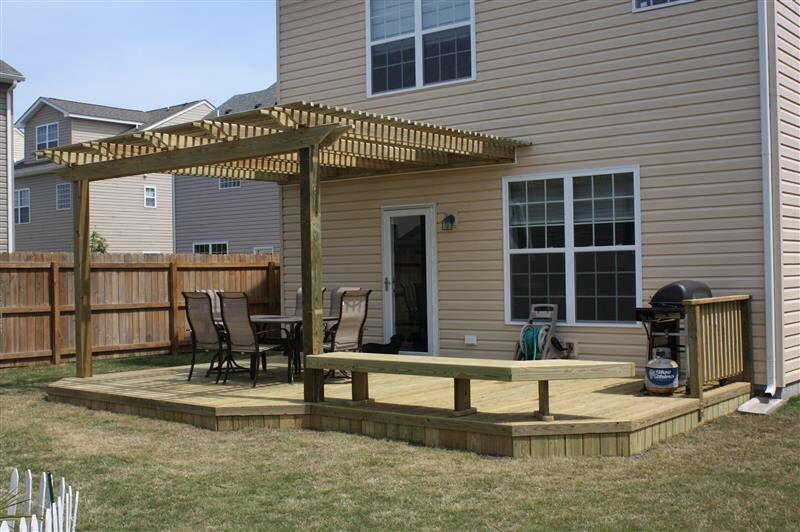 Backyard wooden deck with pergola, patio chairs, and sliding glass door beside a house