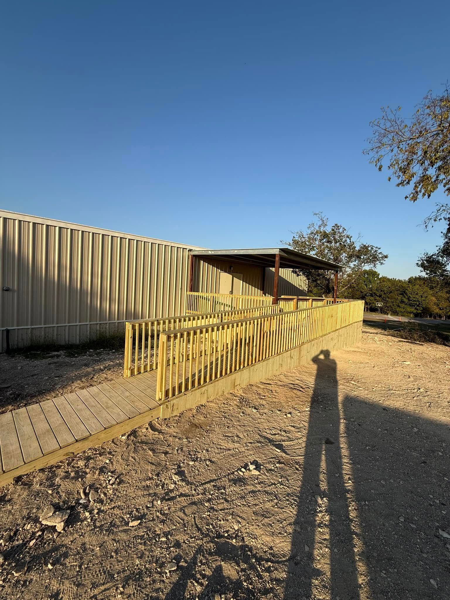 Yellow wooden fence beside a beige building on a gravel lot under a clear blue sky at sunset
