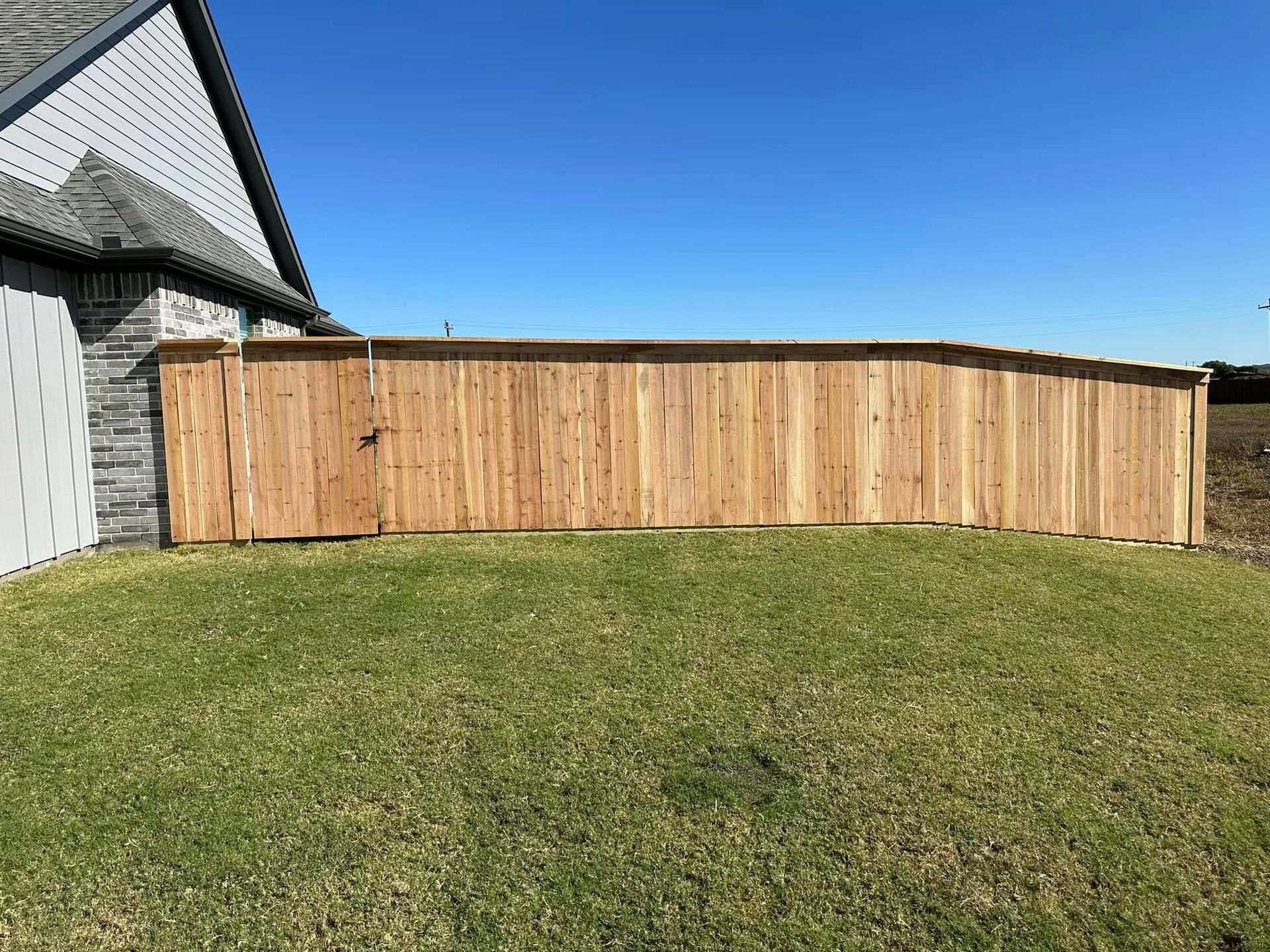 Wooden privacy fence along a grassy yard beside a house under a clear blue sky