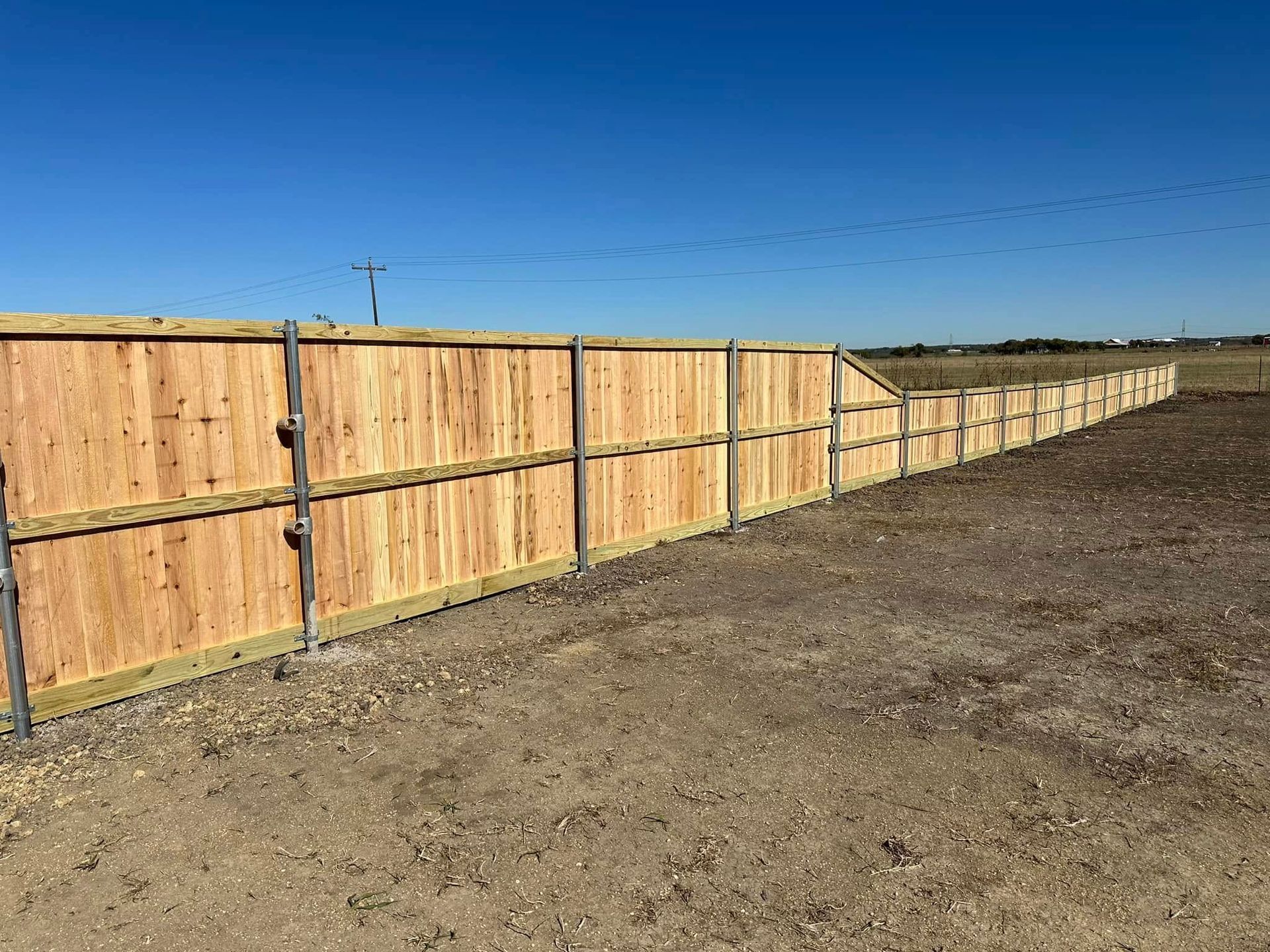 Long wooden fence along a dirt lot under a clear blue sky