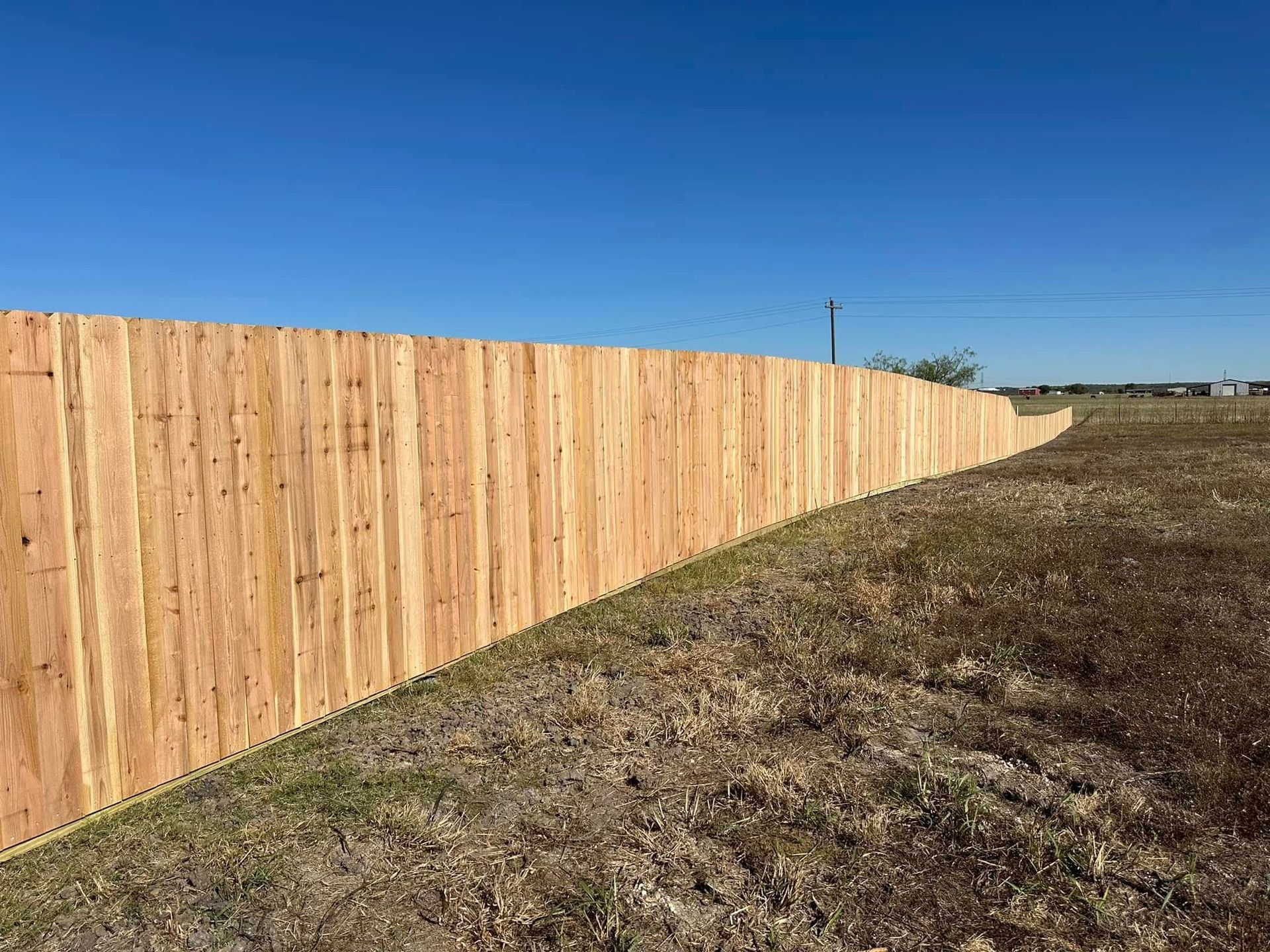 Long wooden fence along a grassy field under a clear blue sky