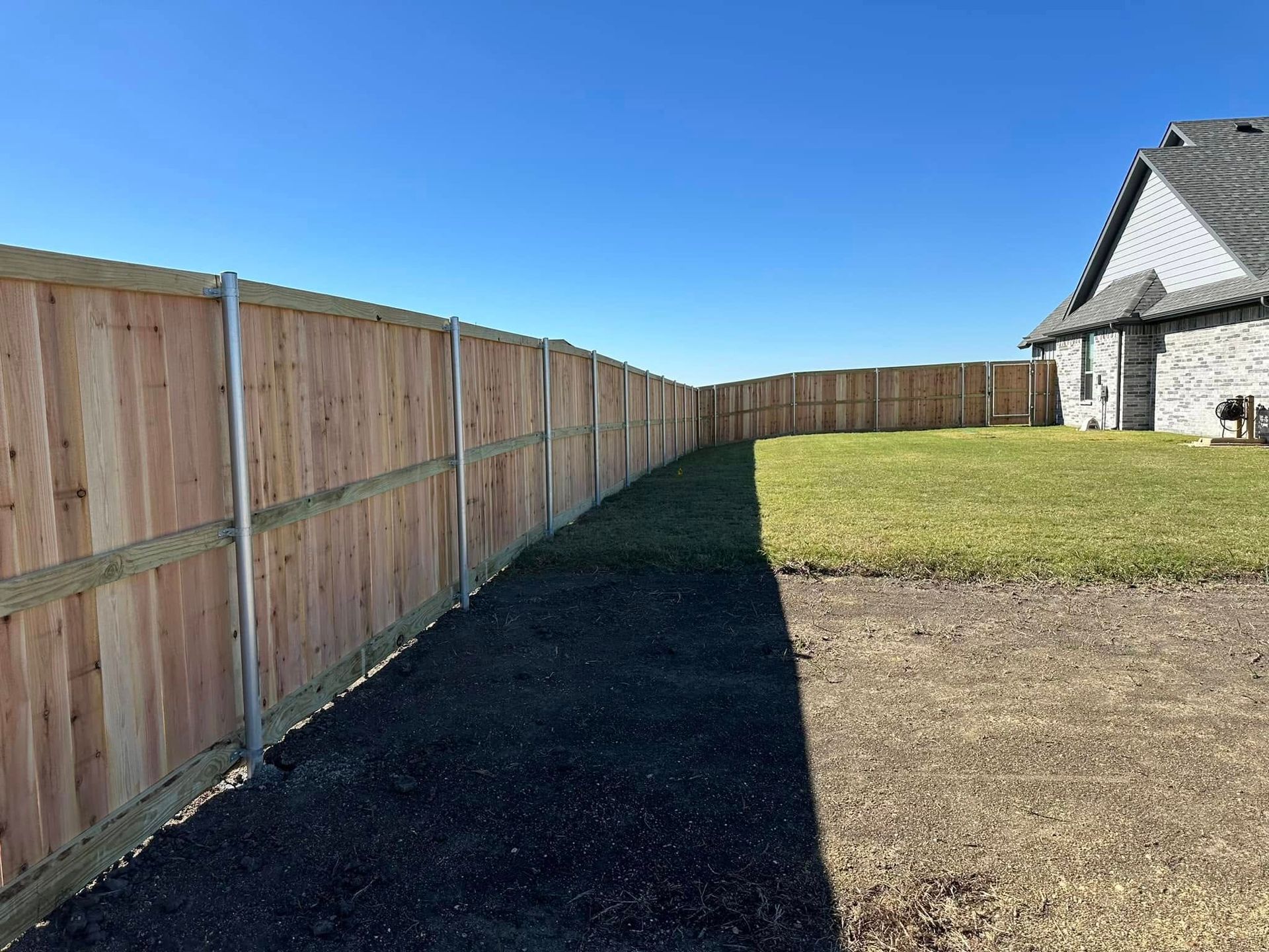 Wooden privacy fence beside a grassy yard and gravel path under a clear blue sky