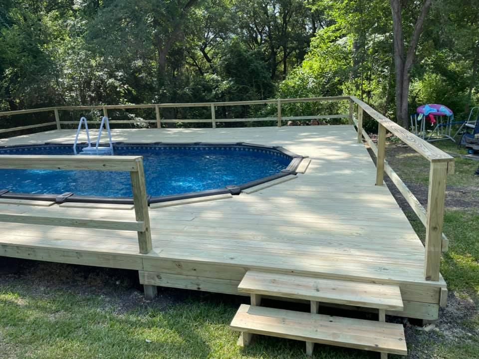 Backyard deck around a blue above-ground pool with steps and railing, surrounded by trees.