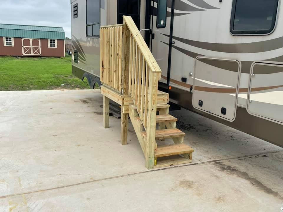 Wooden RV steps with a railing beside a white camper on a concrete pad