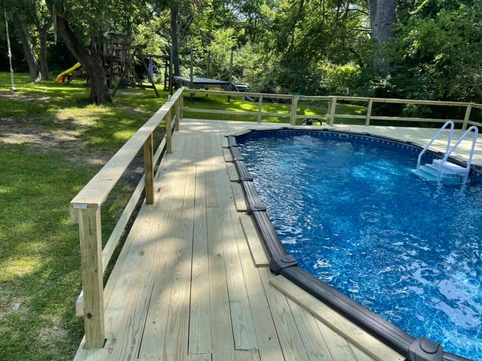 Wooden deck beside a blue swimming pool in a leafy backyard garden