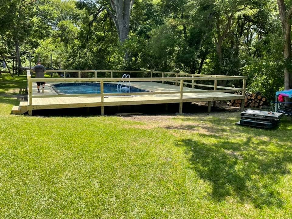 Backyard above-ground pool with wooden deck, surrounded by grass and trees