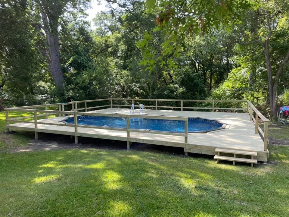 Backyard pool covered by a blue tarp, surrounded by a wooden deck and trees