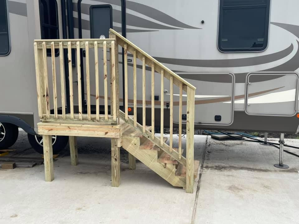 Wooden RV porch and stairs on a concrete pad beside a travel trailer