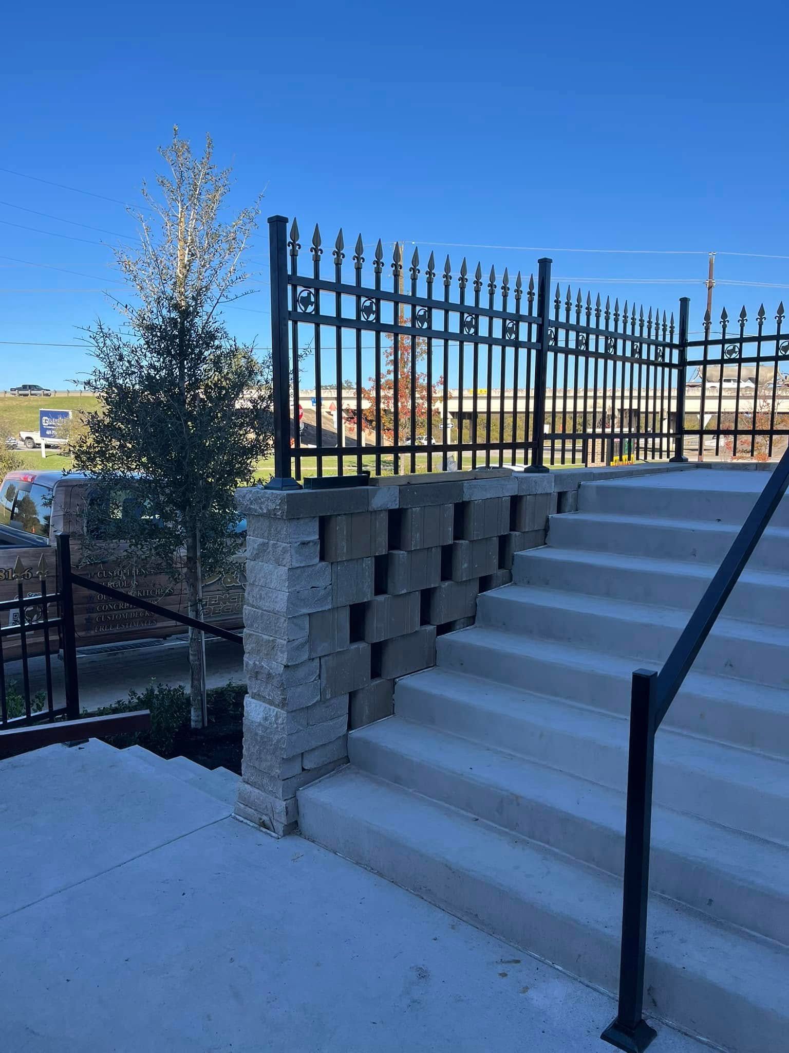 Concrete outdoor stairs beside a black metal fence and retaining wall under a clear blue sky